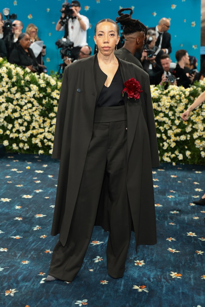 A woman poses on a blue carpet wearing a black tailored suit