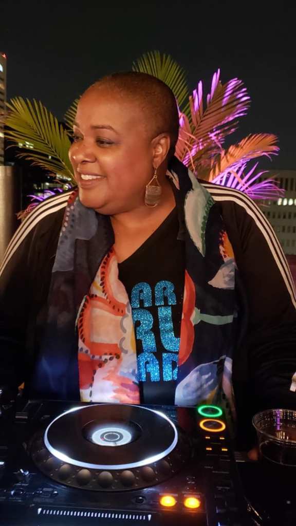 A photograph of a woman with short hair behind the decks. 