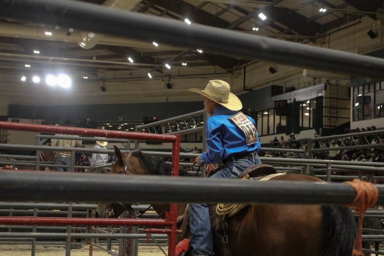 A young competitor waiting to enter the arena in the 35th Annual Bill Pickett Invitational Rodeo. He is wearing a cowboy hat and a blue shirt. 