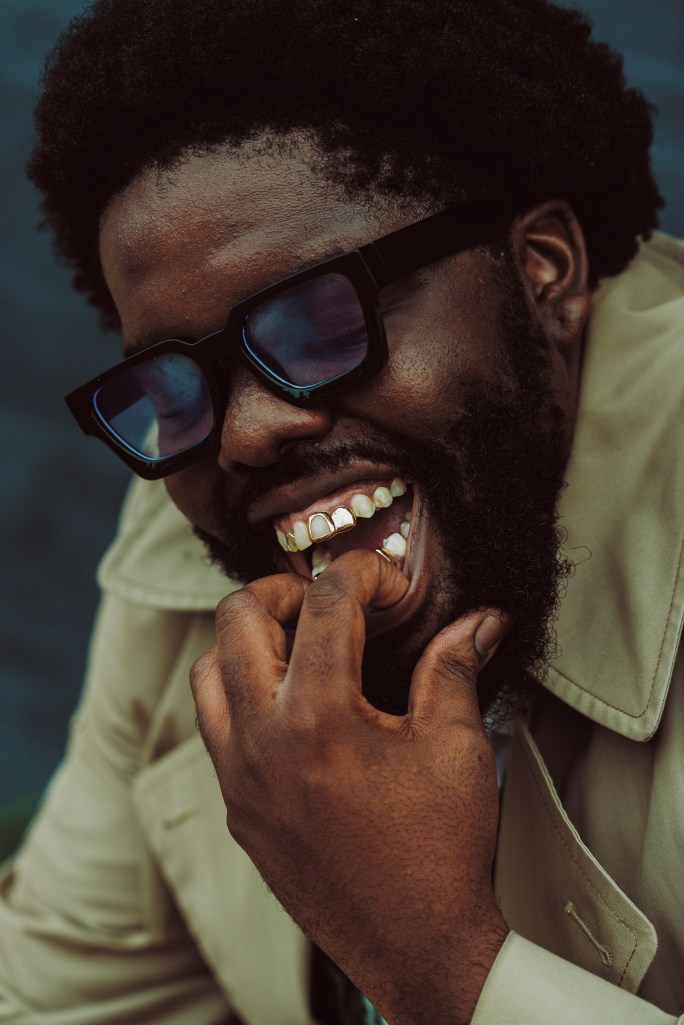 A man with brown skin poses for the camera revealing gold teeth.