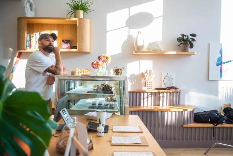 A photograph of a chocolate shop, a person rests on a display case and looks out the window. 