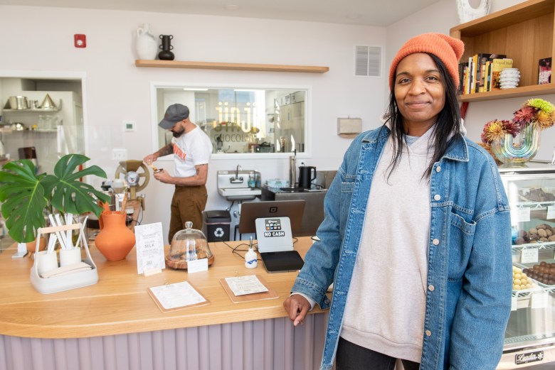 Two figures pose in a chocolate shop. One has brown skin. 