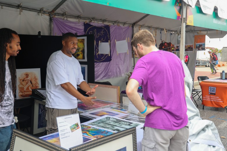 Two people in a booth speak with someone inspecting what they have for sale. 