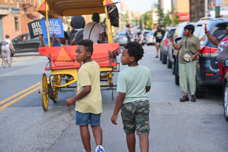 Two young people walk behind a horse-drawn fruit cart. 