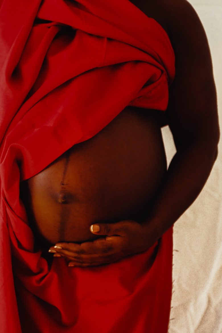 A pregnant person's belly. The person is draped in red. They have dark skin.