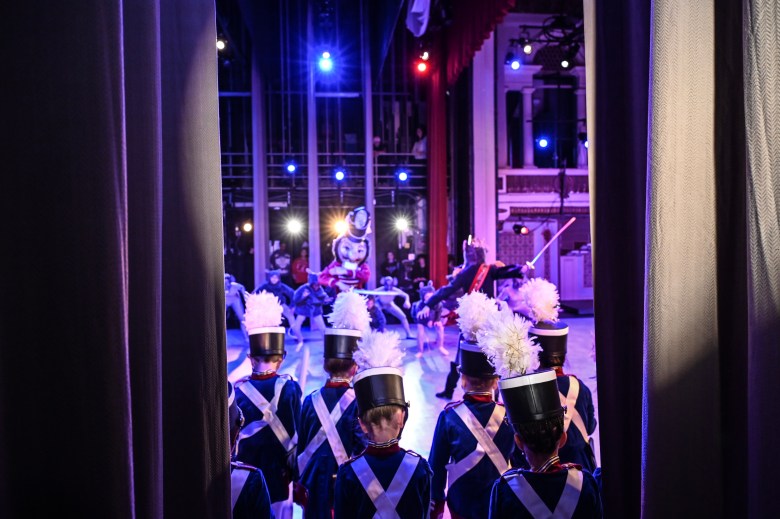 Students dressed as soldiers wait backstage during rehearsal for The Nutcracker. You can see their shoulders and plumed top hats. 