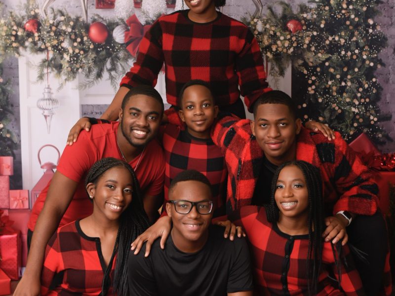 Seven family members pose for a holiday photo. They are wearing matching red holiday pajamas.