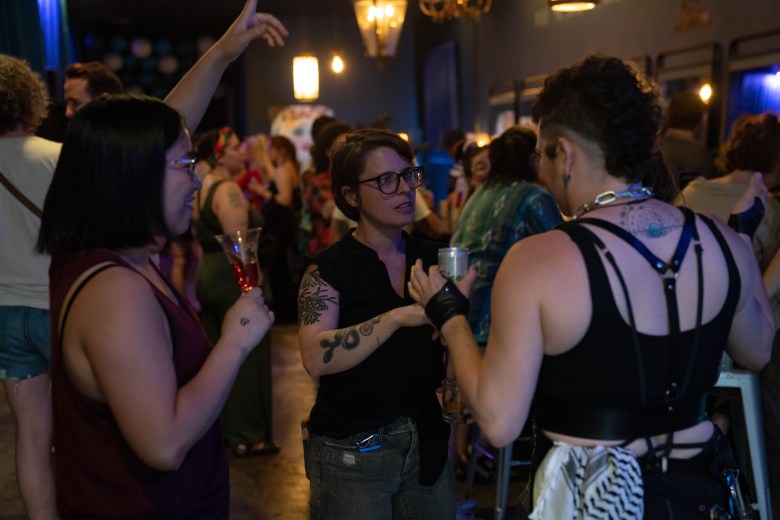 Three people talk while holding drinks. 