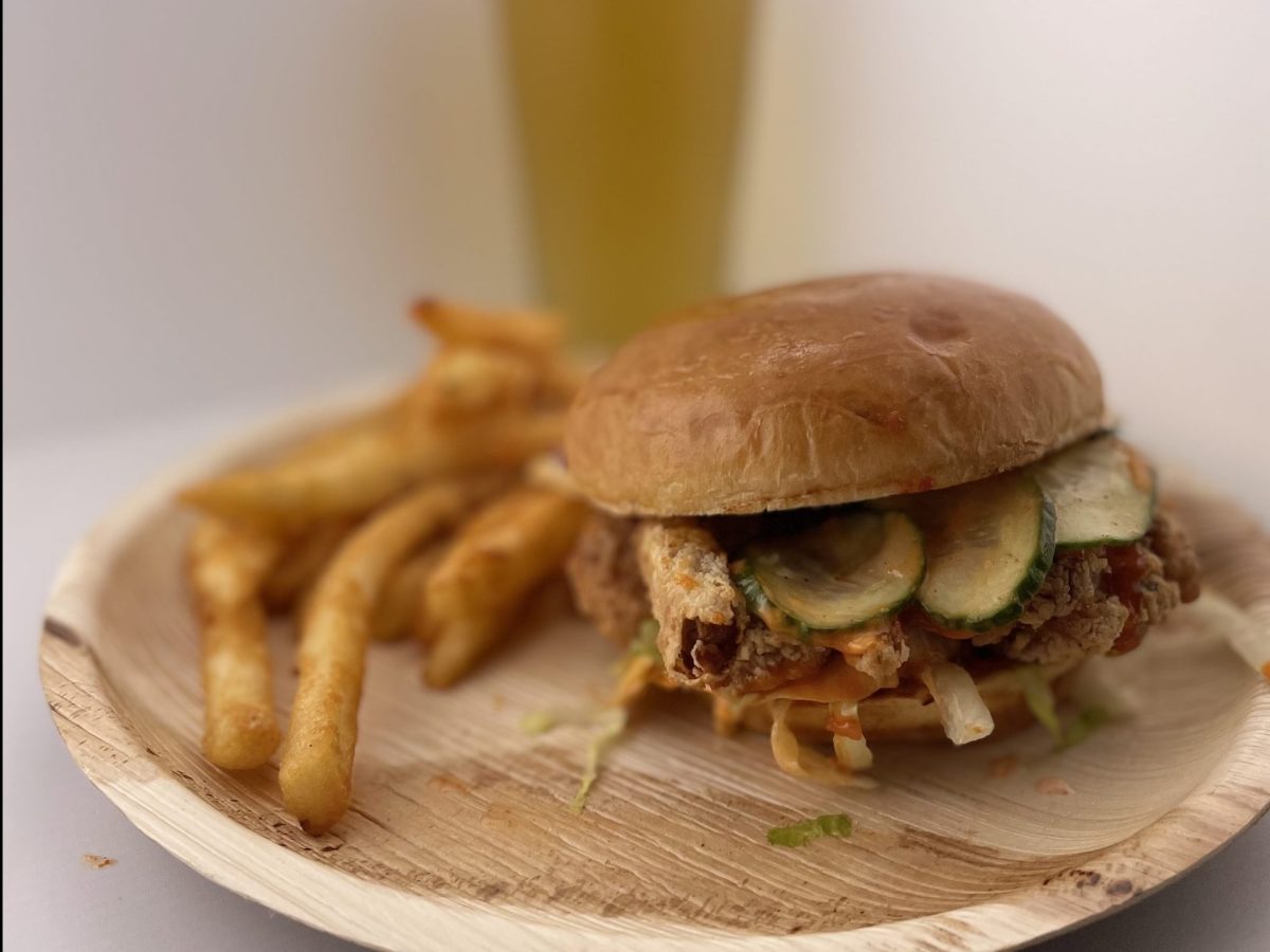 A sandwich and fries on a tan plate with a glass of beer in the background.