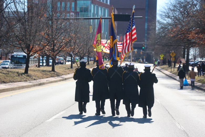 The backs of military members as they hold flags high. 