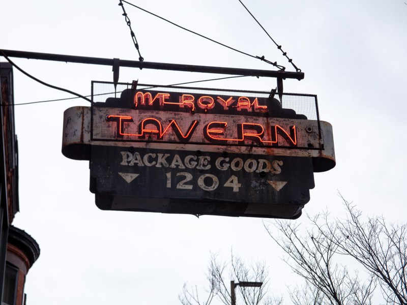 A sign suspended from a building. The sign reads: Mount Royal Tavern
