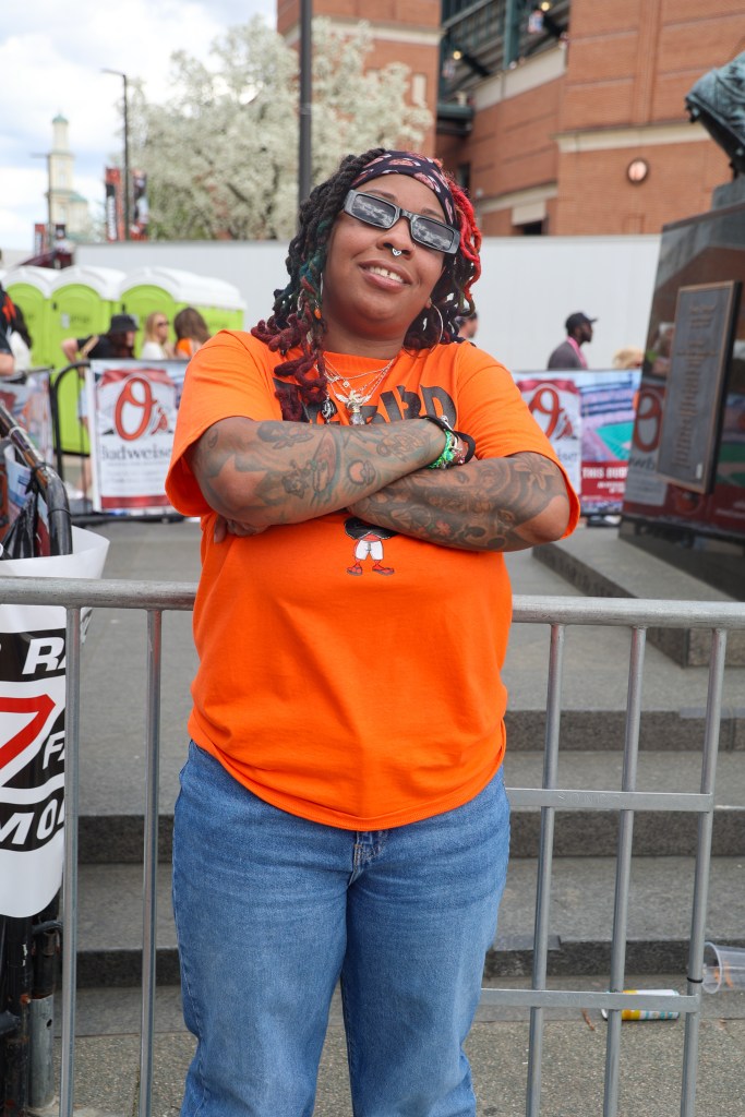 A person poses wearing cool shades, a bright orange t-shirt, and jeans.