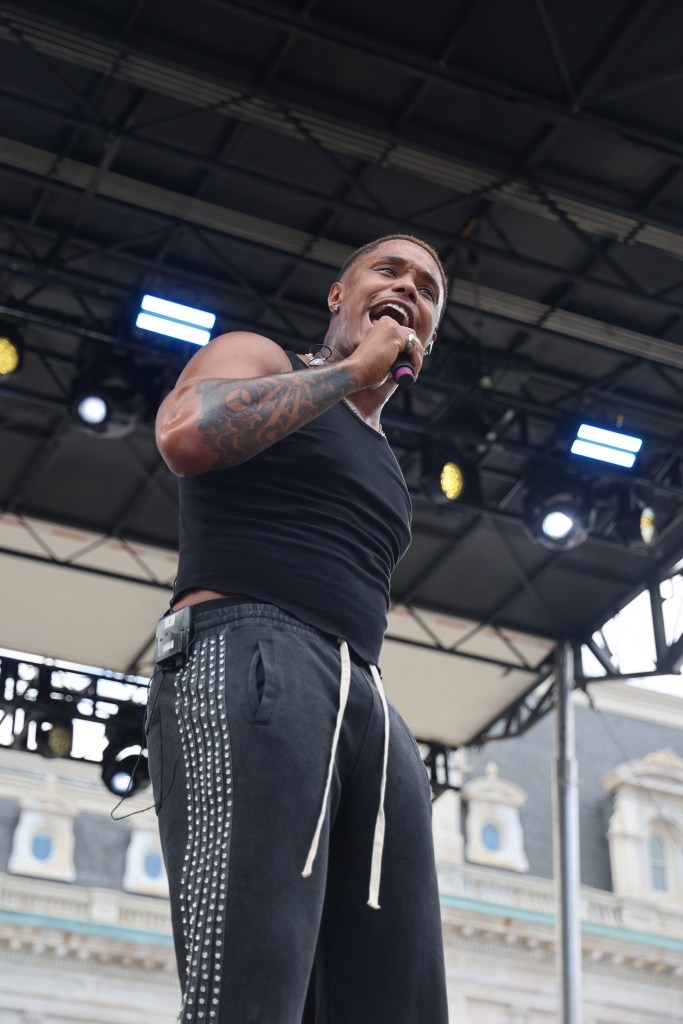 A man in a black tank and sweatpants holds a mic