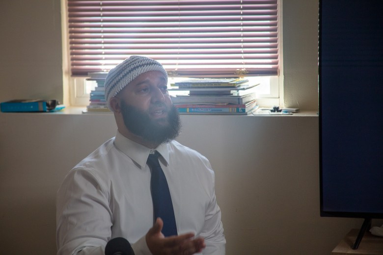 Adnan Syed, a man with a beard, speaks to reporters at his parents home. He wears a white shirt and a dark tie.
