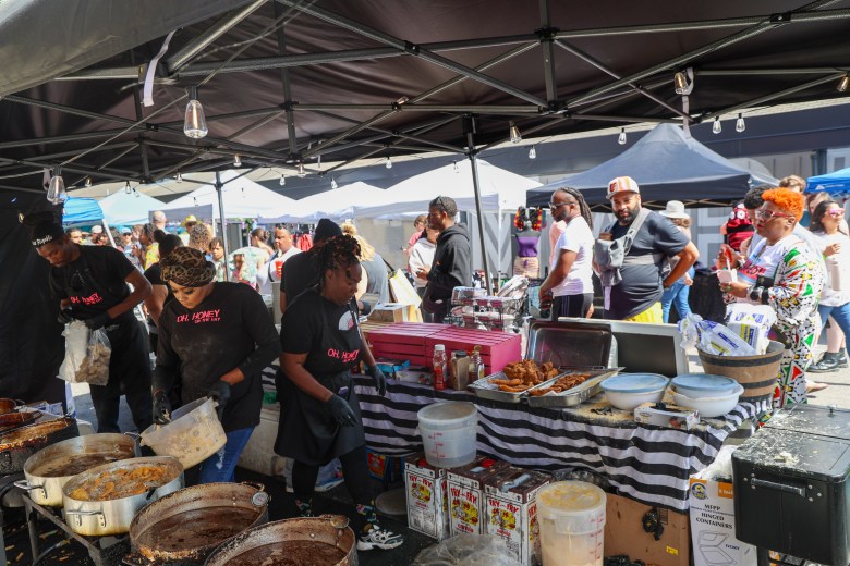 People under a tent cook using large pots of hot cooking oil. Others wait to purchase food.