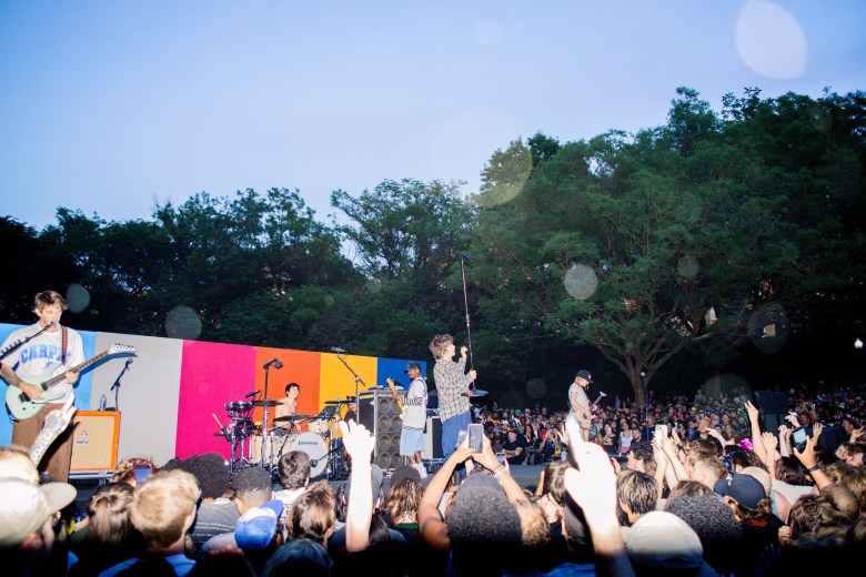 Turnstile performs on stage while surrounded by thousands of fans. They stand in front of a color-block background.